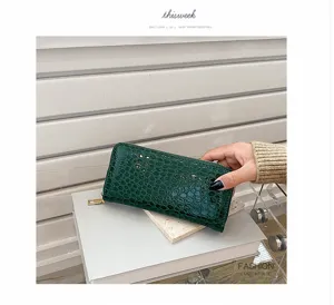 Detalle de la cartera verde oscuro con textura de cocodrilo y cremallera dorada.