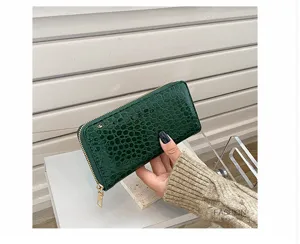 Detalle de cartera larga verde oscuro con relieve de cocodrilo y cremallera dorada