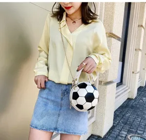 Bolso bandolera único con forma de balón de fútbol llevado por una modelo al aire libre.