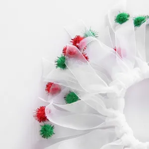 Detail of white mesh pet Christmas collar with red and green tinsel pom-poms.