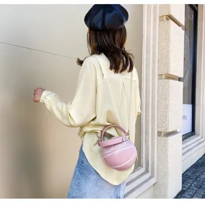Bolso bandolera rosa con forma de baloncesto y cadena, lucido por una modelo en la calle