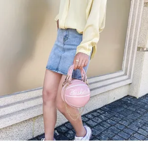 Vista detallada de un bolso rosa con forma de baloncesto y elegante cadena dorada