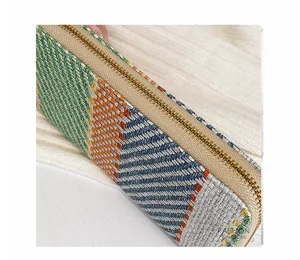Macro view showing the detailed woven fabric and gold zipper of the clutch bag