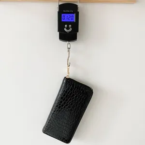 Cartera larga negra con patrón de cocodrilo que pesa 0,120 kg en una báscula digital.
