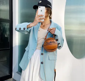 Elegante bolso bandolera con forma de baloncesto naranja y cadena en una modelo.