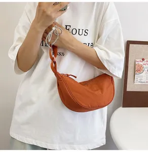 Detalle de un bolso de nailon naranja vibrante con forma de media luna en una modelo