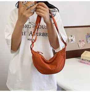 Vista detallada del bolso de media luna de nailon naranja llevado por una modelo casual