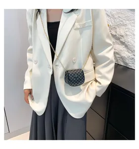 Detalle de un mini bolso bandolera vintage con cadena dorada sobre un blazer blanco