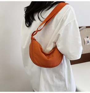 Detalle de un elegante bolso de nylon naranja en forma de media luna estilo bandolera.