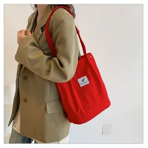 Bolso tote de pana roja mostrado en una modelo con blazer verde para uso diario