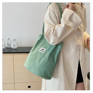 Bolso de hombro grande de pana verde claro llevado por una modelo con abrigo crema