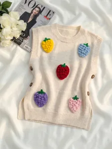 Chaleco de punto crema con parches de fresas en 3D y detalles de botones laterales.