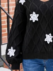 Nahaufnahme Detail des schwarzen Zopfmuster-Pullovers mit weißen Häkel-Schneeflocken.