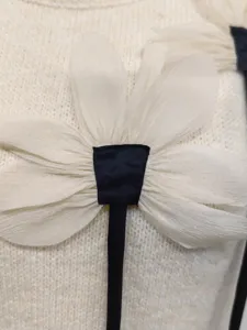 Macro view showing detailed white 3D fabric flower on minimalist beige knitted vest