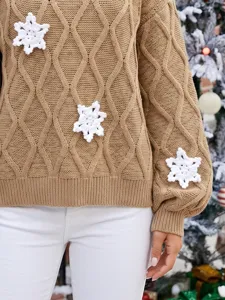 Nahaufnahme des kamelfarbenen Zopfmuster-Pullovers mit handgemachten weißen Häkelsneeflocken.