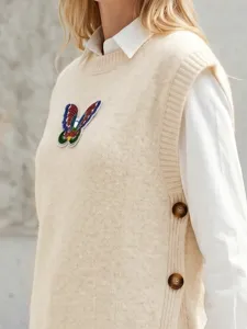Detailaufnahme der beigen Strickweste mit Pailletten-Schmetterling und Seitenknöpfen.