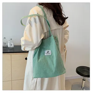 Bolso tote de pana verde menta llevado por una modelo en un entorno minimalista