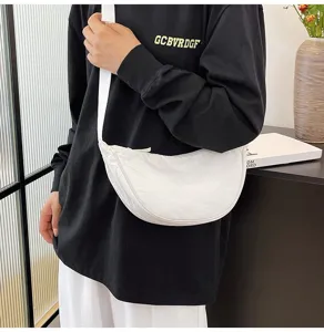 Bolso bandolera de nailon con forma de media luna llevado por modelo, tela blanca.