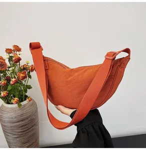 Vista lateral del bolso dumpling de nailon naranja con textura y correa ajustable