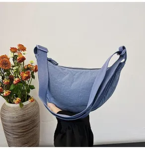 Primer plano de un bolso bandolera de nailon azul en forma de media luna sostenido con la mano