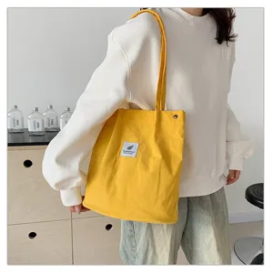 Vista detallada de un bolso de pana amarillo llevado por una modelo en un interior.