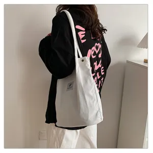 Bolso tote minimalista de pana blanca que se lleva al hombro sobre camiseta negra.