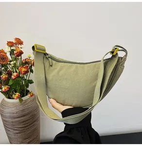 Primer plano de un bolso de media luna de nailon verde sostenido en la mano, detalle suave.