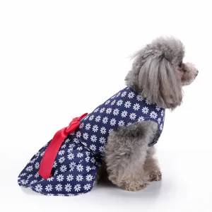Side view of small dog wearing a blue daisy print summer dress with a vibrant red bow detail