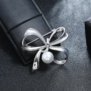 Detail view of a vintage silver metal bow brooch with a central white pearl.