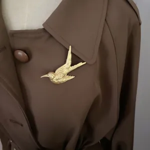Detailansicht einer matten goldenen Vintage-Vogelbrosche an einem braunen Mantel