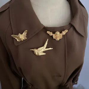 Nahaufnahme von vintage mattgoldenen Broschen mit Relief-Vogel- und Puttenmotiven