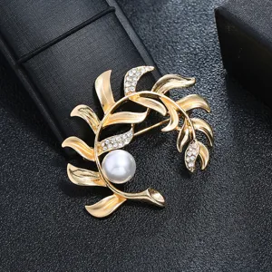 Close-up of a vintage gold leaf brooch with crystals and a white pearl detail.