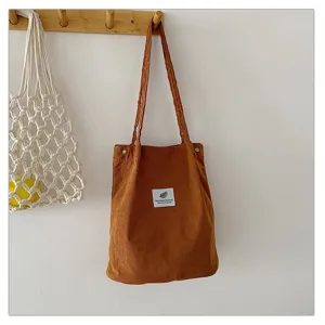 Bolso tote minimalista de pana marrón colgado en un perchero de pared de madera.