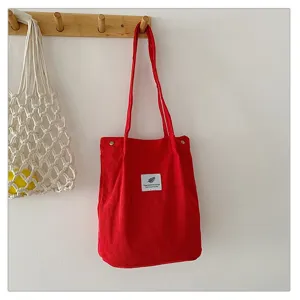 Bolso shopping de pana roja con etiqueta minimalista colgado en gancho madera