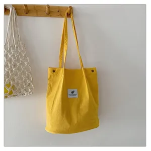 Bolso de pana amarillo colgado en un gancho de madera, mostrando su textura suave