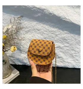 Primer plano de un bolso bandolera vintage marrón con cadena sostenido contra una pared.