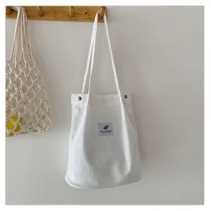 Vista detallada de un bolso shopper de pana blanca con textura suave en un gancho de madera.