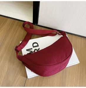 Detalle de bolso bandolera de nailon burdeos sobre una revista blanca minimalista
