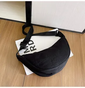 Primer plano de un bolso bandolera de media luna de nailon negro sobre un libro blanco