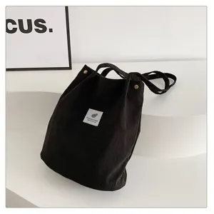 Detalle de un bolso de hombro minimalista de pana marrón oscuro con parche de hoja