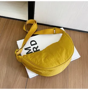 Vista detallada de bolso bandolera de nailon amarillo con tejido texturizado sobre un libro