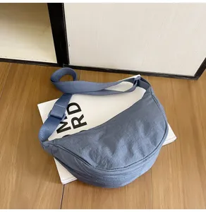 Detalle de un bolso bandolera de nailon azul en forma de media luna sobre madera