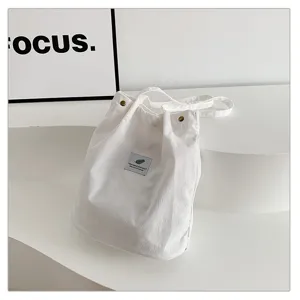 Primer plano de bolso tote de pana blanca con textura suave y parche de logotipo minimalista.