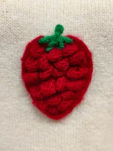 Detalle de bordado de fresa en 3D en un chaleco de punto color crema para mujer