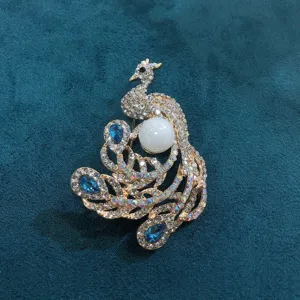 Elegant peacock brooch featuring sparkling blue rhinestones and a large white pearl center.