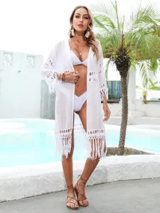 Full-body view of a white crochet beach cover-up with tassels in a resort pool setting