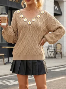 Detailed shot of a beige diamond knit sweater featuring 3D floral appliqués on V-neck.
