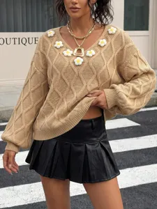 Close-up of beige knit sweater featuring 3D daisy crochet flowers, V-neck and lantern sleeves.