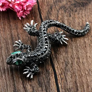 Vintage lizard brooch featuring black rhinestones and green crystal eyes on wood.