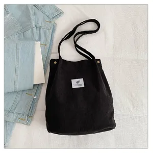 Vista detallada de un bolso tote de pana negra minimalista con una etiqueta blanca decorativa